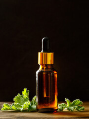 Geranium essential oil in dark glass bottle with fresh scented geranium leaves on old wooden board...
