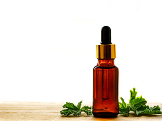 Geranium essential oil in dark glass bottle with fresh scented geranium leaves on old wooden board isolated on white background. Aromatherapy oil, spa massage, mosquito repellent. Copy space
