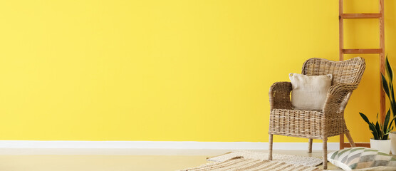 Wicker armchair with cushions, houseplants and ladder near yellow wall with space for text