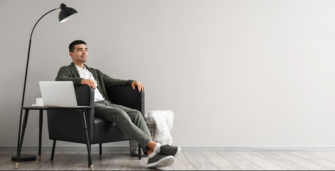 Young man sitting in black armchair near light wall with space for text