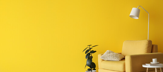 Interior of living room with yellow armchair, table, houseplant and lamp near yellow wall with...