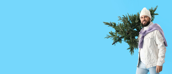 Handsome man with Christmas tree on light blue background with space for text
