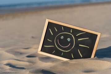 Una pizarra con marco de madera y un dibujo hecho a mano de un sol sonriente., en una playa en...