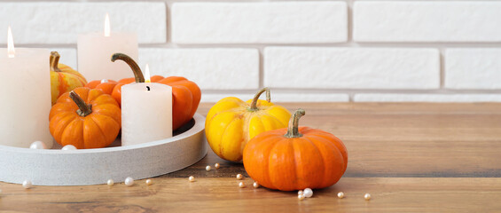 Composition with pumpkins and burning candles on wooden table near light brick wall