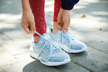 Woman in stylish sneakers tying shoe lace outdoors