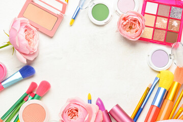 Frame made of decorative cosmetics, brushes and flowers on light background