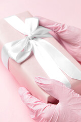 Female doctor in medical gloves holding gift box on color background, closeup