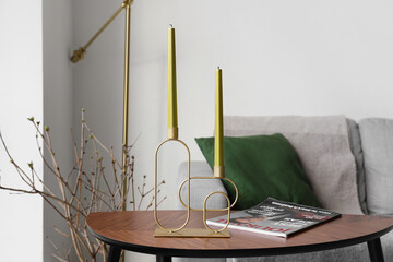 Stylish holder with candles and magazine on wooden table near sofa