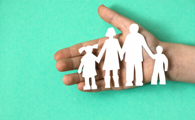 Fototapeta na wymiar paper cut family in child's hand, green background. child care, guardianship and adoption concept. family violence against children. orphanage
