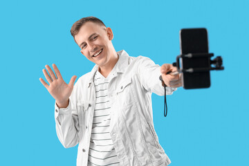 Naklejka premium Young man with mobile phone taking selfie on blue background