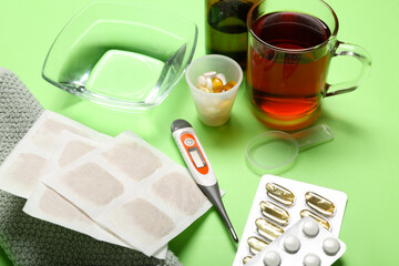 Mustard plasters with medicines, cup of tea and towel on green background