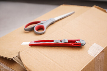 Utility knife with scissors on cardboard box, closeup