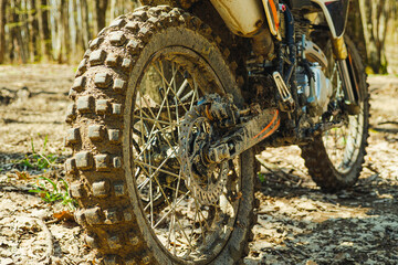 Dirty back wheel of a motorcycle with off-road tread. Cross bike in the woods. Large wheel tread. Selective focus. Blurred background. Extreme sport.