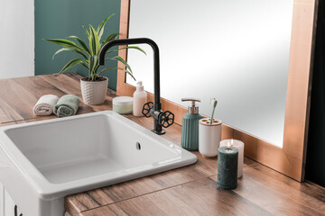 Fototapeta na wymiar Bath accessories with houseplant, sink, burning candles and mirror on table near wall