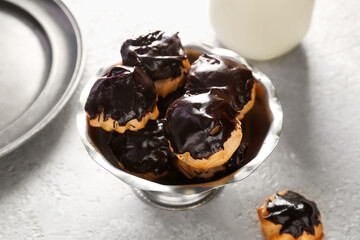 Bowl with delicious eclairs on light background