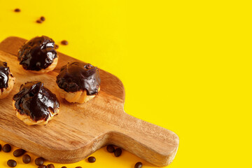 Wooden board with tasty eclairs on yellow background