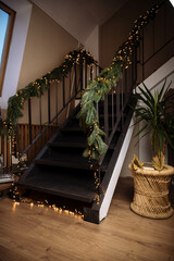 Details of the house, metal stair railings are decorated with artificial spruce branches, a Christmas tree and a garland of golden lights. The concept of the idea of the interior decor of a Christmas 