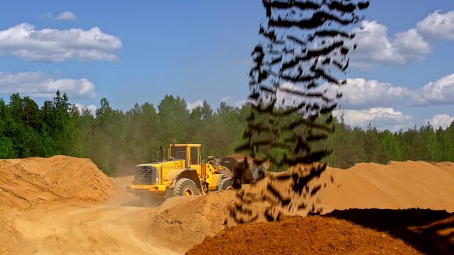 Soil Pouring In Slow Motion With Wheel Loaded Transporting Aggregates In Background. wide