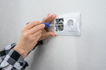 Hand with screwdriver for repairing electrical outlets at home. Electrician is using screwdriver to install power outlet in to plastic box on white wall.