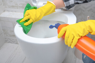 Close up hand with detergent cleaning toilet. Cleaning service. close up hands wearing yellow protect glove using liquid cleaning solution cleaning flush toilet, disinfection and hygiene concept