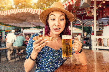 Hungry and funny girl drinking beer and eating traditional german currywurst meal at funfair and street food festival. National cuisine and biergarten concept