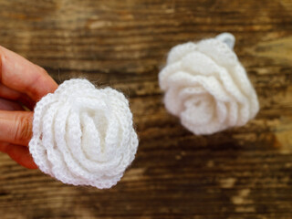 Close up Crochet white rose flower in woman hand on old wooden background, hand made concept. Horizontal, top view