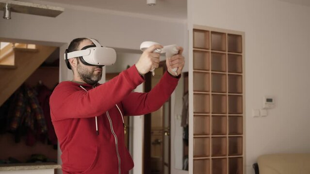 Man Playing VR Shooter Game With Virtual Reality Guns and Glasses. Man Wearing Virtual Reality Headset Holding Gaming Controllers Swinging Hands, Shooting Dodging Obstacles Metaverse Oculus Technology