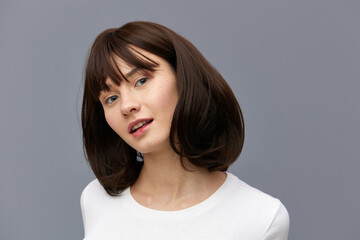 Fototapeta premium a sweet, beautiful, happy woman smiles pleasantly looking at the camera standing on a gray background in a white T-shirt