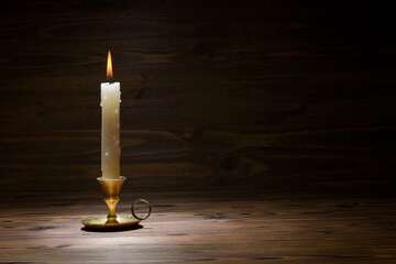 burning old candle with vintage brass candlestick on wooden background in minimalist room interior,copy space