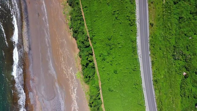 Aerial of cars driving on a highway next to a sandy beach and a beautiful sea with big foamy waves