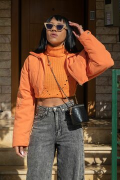 Vertical Shot Of A Young Fashionable African American Woman In An Orange Jacket And Gray Baggy Jeans