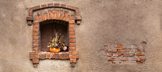 Małe okienko ozdobione bukietem jesiennych kwiatów i dynią w ceglanym budynku