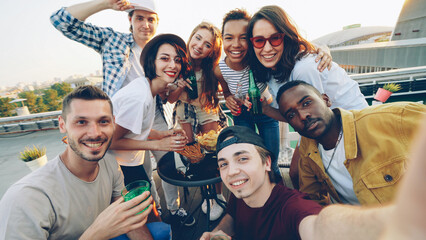 Point of view shot of attractive young men and women taking selfie with bottles, enjoying soft...
