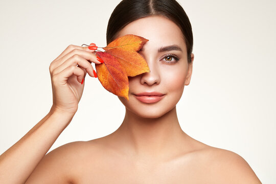 Portrait of beautiful young woman with autumn leafs. Healthy clean fresh skin natural make up beauty eyes and red nails