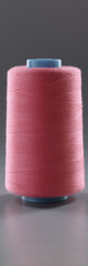 Thread for dressmaking, pink colour thread spool on grey surface, yarn for sewing