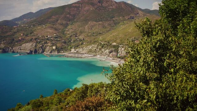 Stunning reveal dolly shot of colorful bay area, coastline and town of Levanto from behind a tree during a lovely, sunny afternoon. Italy, Mediterranean Sea Coast, Europe