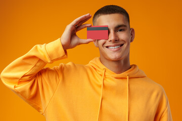 Handsome young man holding credit card on yellow color background