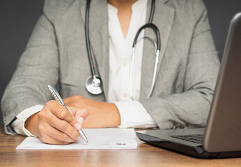 A doctor in a suit holding a pen writing on a medical prescription while sitting in the hospital
