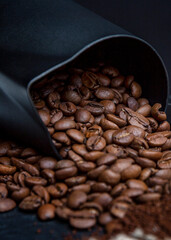 Roasted coffee beans spilled out of the black milk jug. Preparation of aromatic drink. Close-up. Vertical. Dark background.