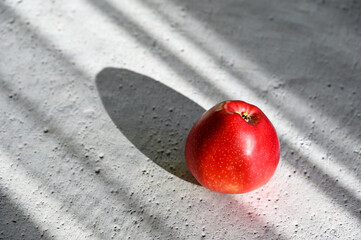 The sun shines on a red apple that lies on the table 