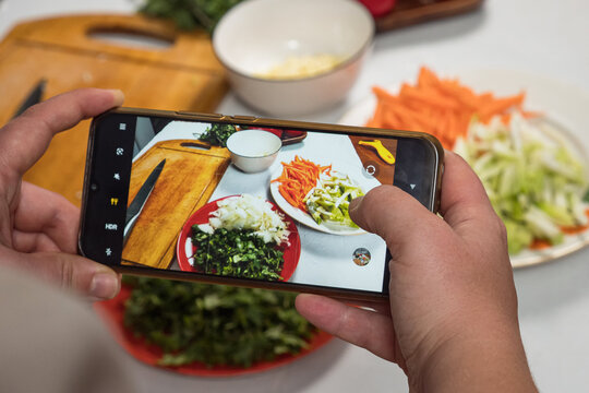 A female blogger's hands take pictures on her smartphone of vegetables sliced on the table. The sliced vegetables are beautifully arranged on plates.