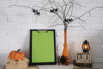 Decorative composition for the holiday of Halloween. A pumpkin, a calendar, a flashlight, a spider, a vase in branches on which bats sit lie on the table. A place for your text against a white brick - Powered by Adobe