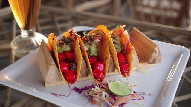 Delicious tacos with red paneer close-up. A married woman takes a delicious tacos from a white plate on the background of a table with a drink and rattan cafe furniture