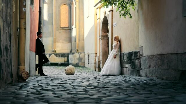 Wedding in the city. The bride and groom stand opposite each other on a cozy street. Wedding brides on different sides of the street.