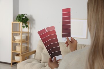 Woman choosing color for wall in room, focus on hands with paint chips. Interior design
