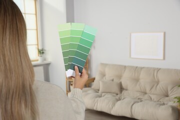 Woman choosing color for wall in room, focus on hand with paint chips. Interior design
