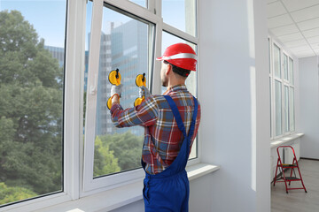 Worker using suction lifters during plastic window installation indoors