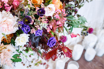 Lush floral arrangement of fresh flowers and greenery on wedding table and candles on floor. Pink, red, purple flowers - roses, lisianthus, hydrangea. Close-up, selective focus.
