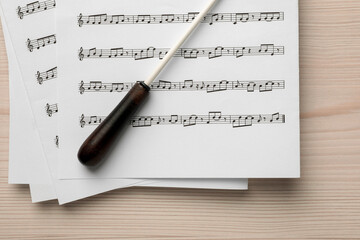 Conductor's baton and sheet music on white wooden table, top view