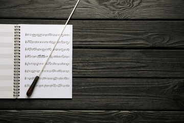 Conductor's baton and sheet music book on black wooden table, top view. Space for text